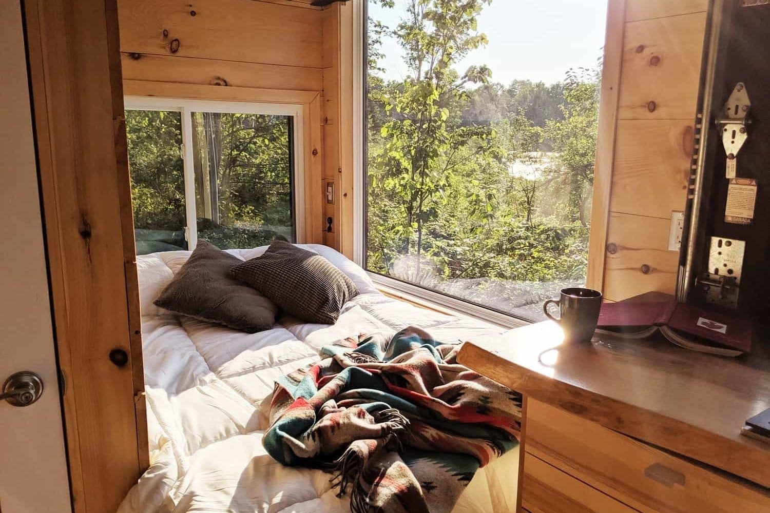 Cozy wooden cabin bedroom with large window overlooking forest and water view