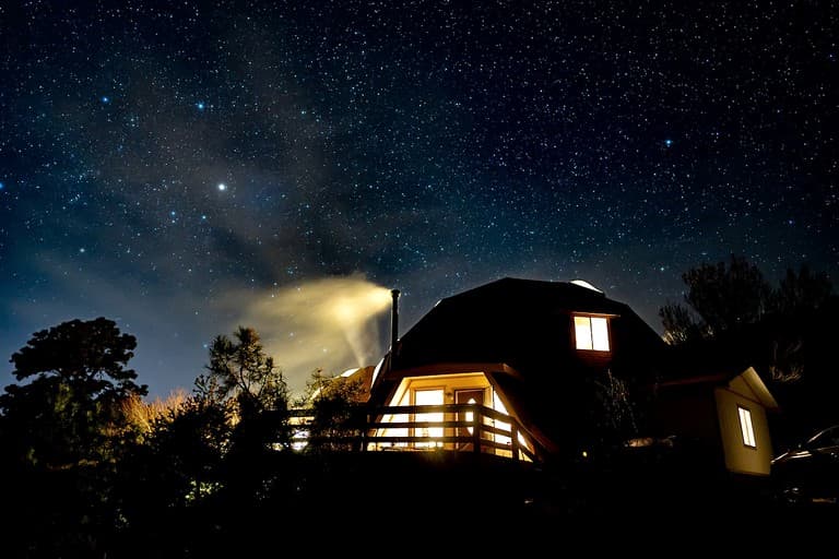 Illuminated dome structures under starry night sky with searchlight beam