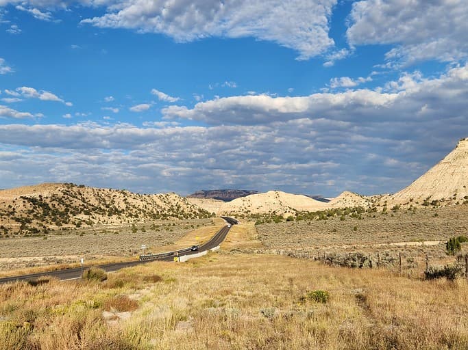 Modern cabin nestled in wide desert valley with road, sagebrush, and mountains under blue sky