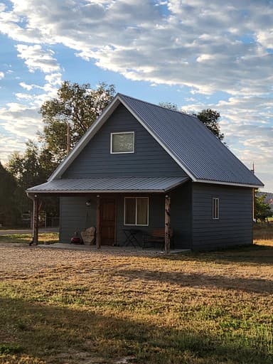 Side angle of modern cabin with metal roof, covered porch, and surrounding sagebrush landscape