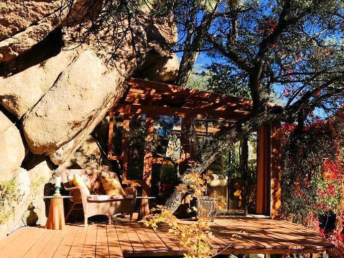 Wooden deck with pergola, lounge seating, and mountain boulders in dappled sunlight