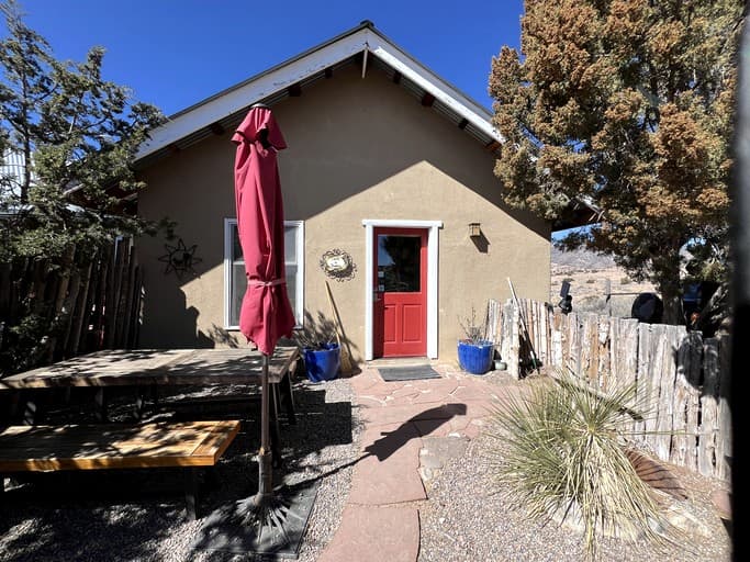 Casita exterior with red door, pink umbrella, and desert vegetation under blue sky