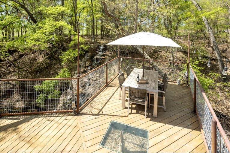 Wooden deck with umbrella and seating overlooking forested landscape in daylight