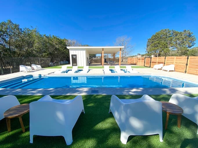 Resort swimming pool with white lounge chairs and modern poolside structure under blue sky