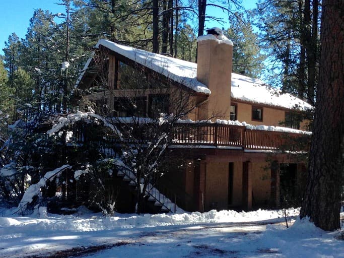 Rustic cabin with brown exterior, snow-covered roof, and wooden deck in forest