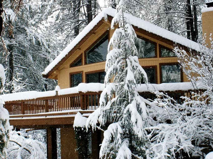 Modern A-frame cabin with large windows surrounded by snow-laden evergreen trees