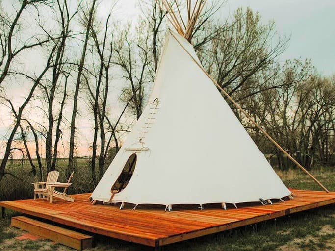 Tipi on wooden platform surrounded by trees at dusk