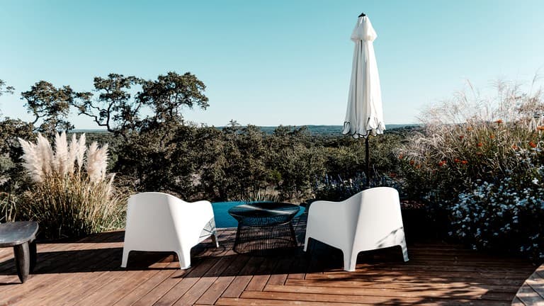 Wooden deck with white modern chairs overlooking savanna landscape at sunset