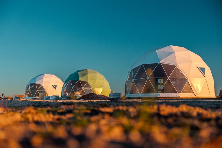 Three geodesic dome structures at sunset with desert landscape in foreground