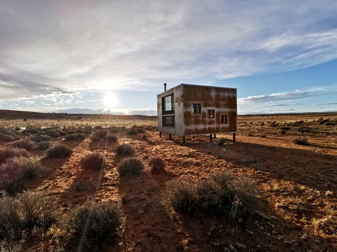 Modern cubic cabin on stilts in desert scrubland with clear sky