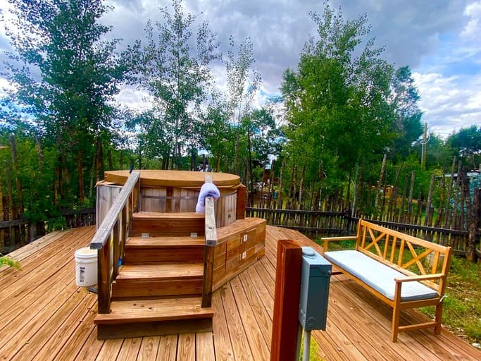 Wooden deck with rustic hot tub structure surrounded by tall evergreen trees