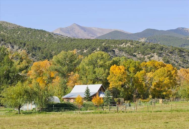 Cabin with white roof nestled in valley surrounded by golden aspens and mountains