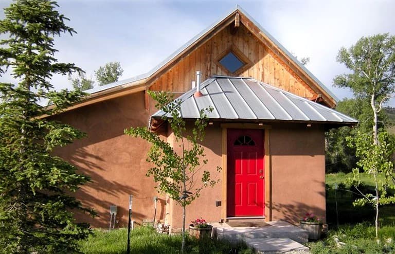 Rustic cabin with red door, pitched roof, and metal roof in natural setting