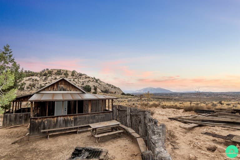 Rustic wooden cabin on desert landscape with mountain in distance at sunset