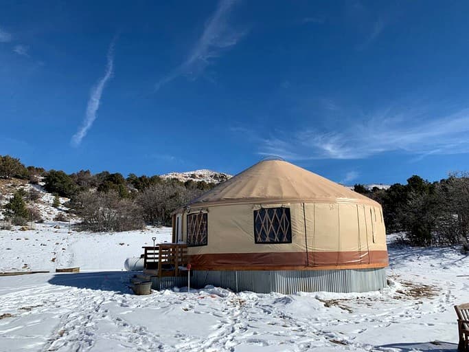 Beige yurt with brown trim on snowy ground under clear blue sky